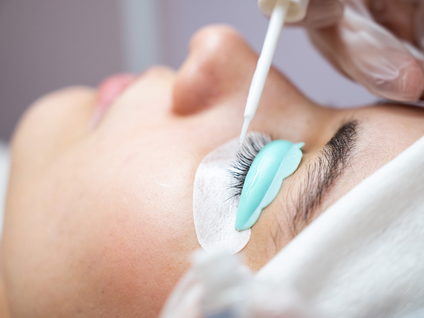 Young woman undergoing eyelash tinting and lamination procedure.